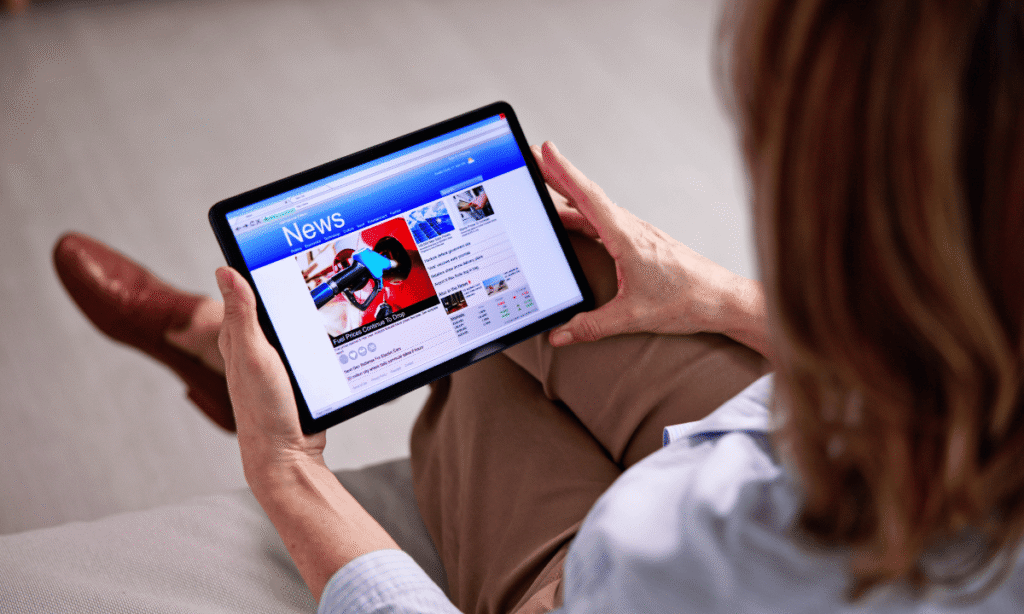 Person holding a tablet displaying a news website with multiple article thumbnails and headlines, illustrating traditional news consumption on digital devices.